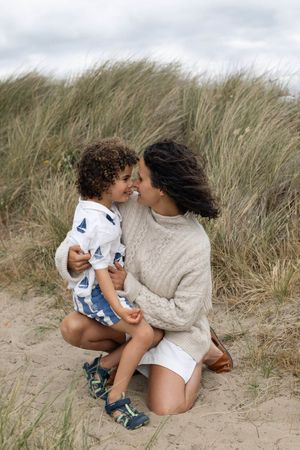 A mother and young child share a tender nose-to-nose moment on sandy beach dunes during a family photography session in Sussex