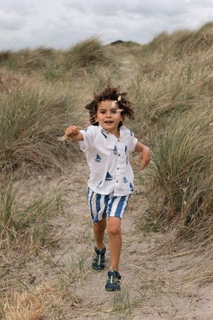 Curly-haired boy running on sandy beach path during a family portrait session in Sussex