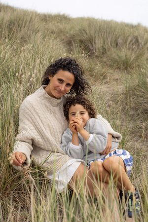 A woman and child sitting together on a grassy sand dune during an outdoor family photoshoot in Sussex