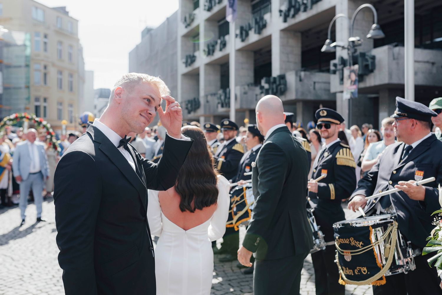 Bride and groom share a joyful moment outdoors with a marching band performing in the background on their wedding day.