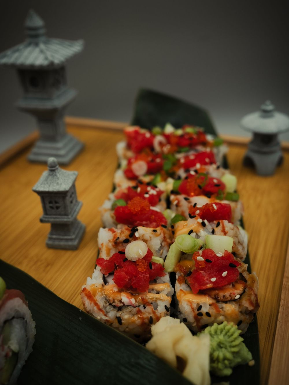 Elegant sushi rolls topped with red tobiko, avocado, and sesame seeds on bamboo tray with decorative Japanese stone lanterns.