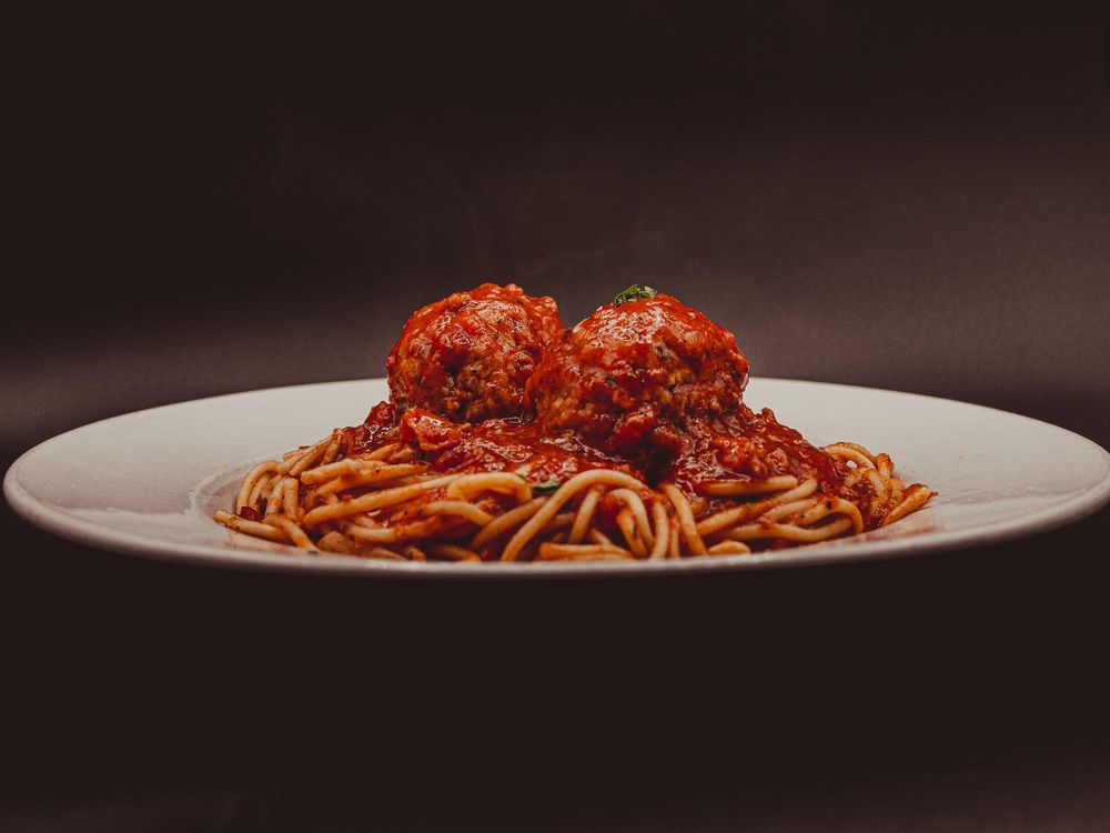 A classic plate of spaghetti topped with marinara sauce and three large meatballs served on a white dish.