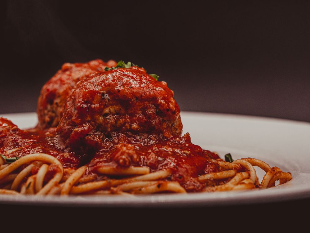 A close-up of spaghetti topped with a large meatball smothered in rich tomato sauce on a white plate.