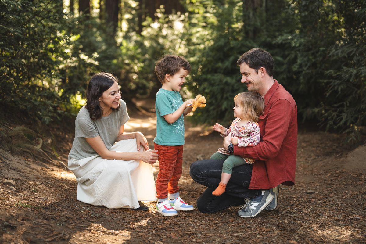 Family enjoying golden hour sunset on a dirt path, parents smiling as young girl in white dress twirls toward them.
