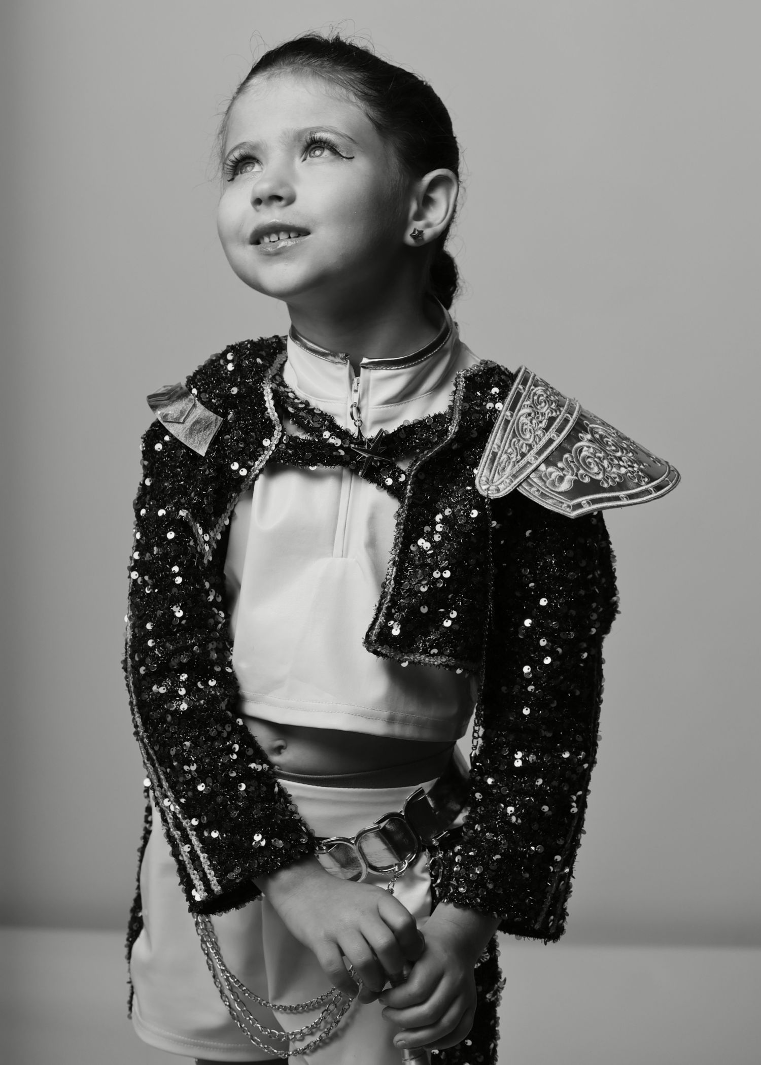 Young girl in sequined black jacket with shoulder detail poses confidently in black and white portrait photo.