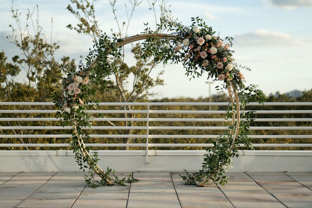 Circular wedding arch adorned with lush greenery and blush pink roses on an outdoor rooftop venue.