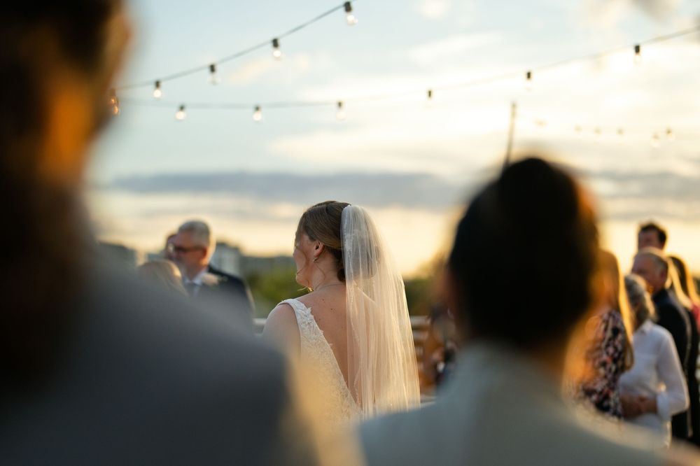 Bride with veil at outdoor wedding reception under string lights at sunset.
