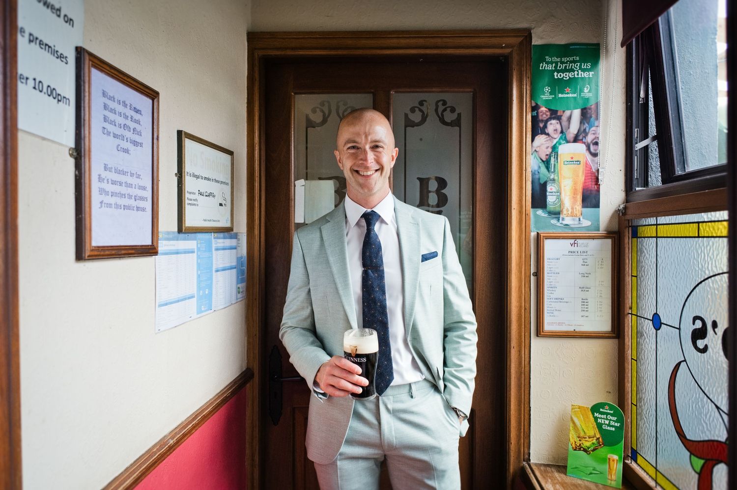 Man in light suit holding a pint of Guinness smiling in a pub doorway.