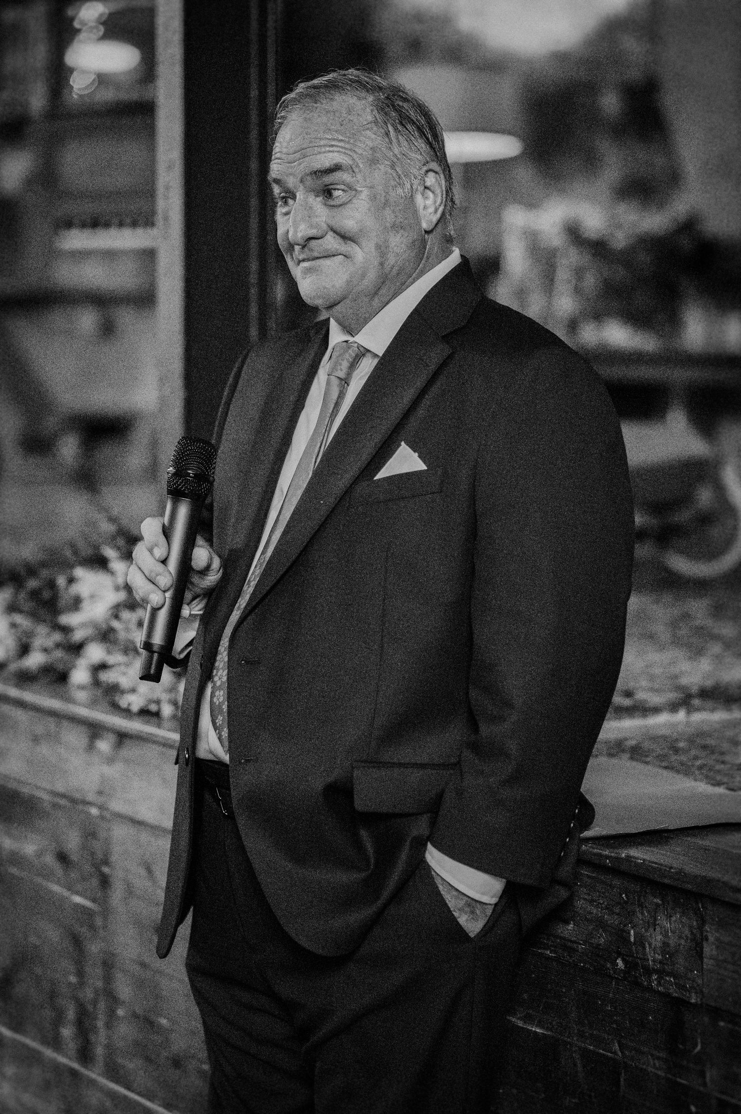 Elegant man in suit holding microphone at wedding reception, black and white portrait photography.