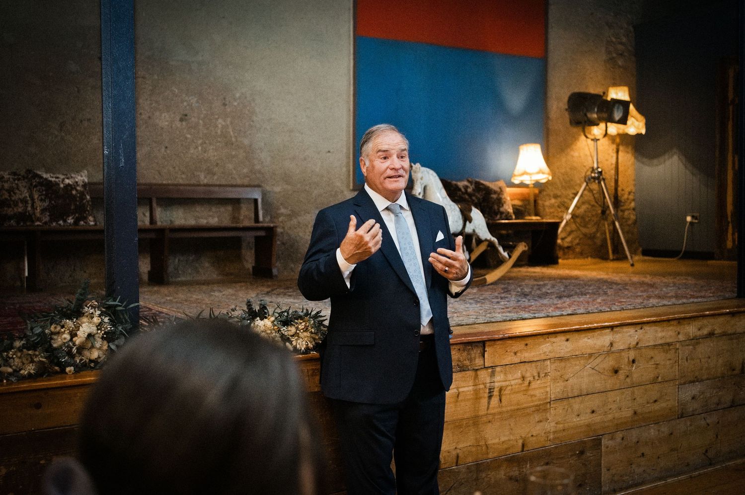 Older gentleman in navy suit gives a heartfelt speech at an elegant wedding reception.