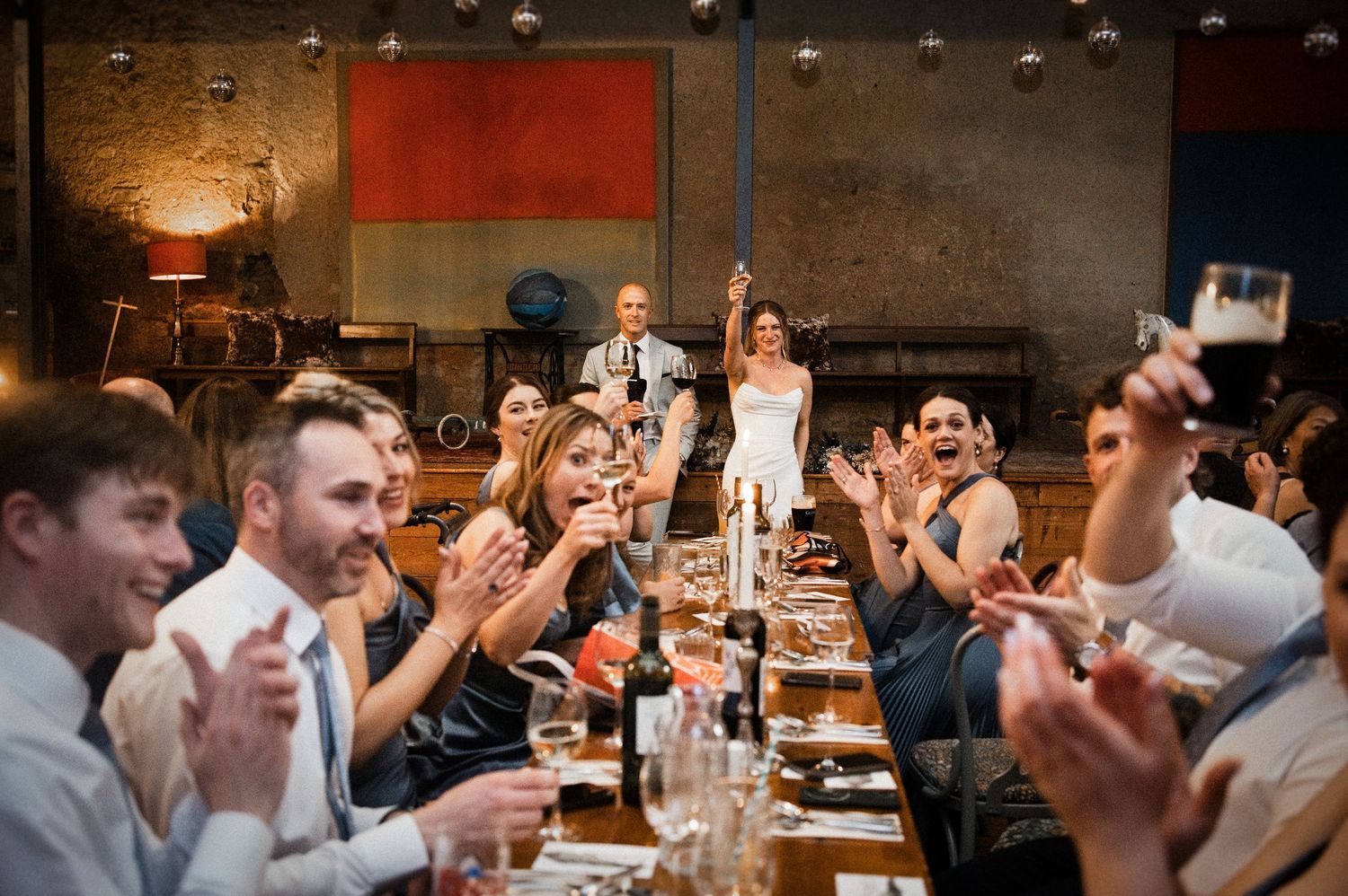 Joyful wedding guests cheer and applaud as bride and groom celebrate at reception.