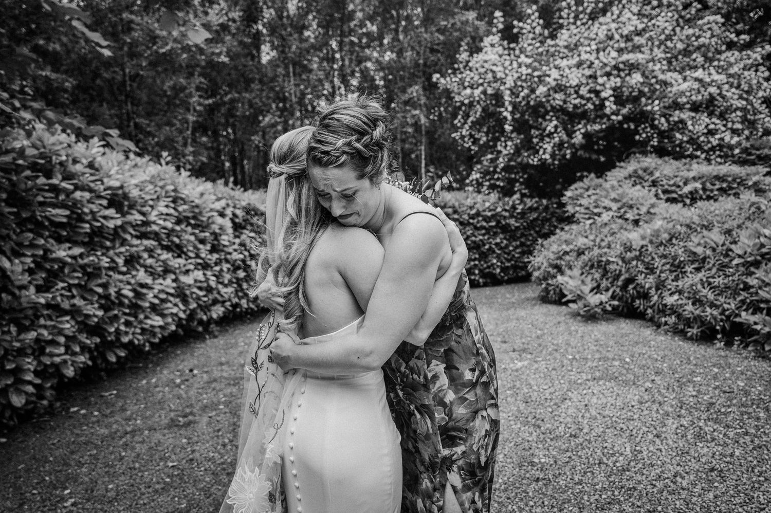 Bride shares an emotional embrace with a loved one in a lush garden setting on her wedding day.