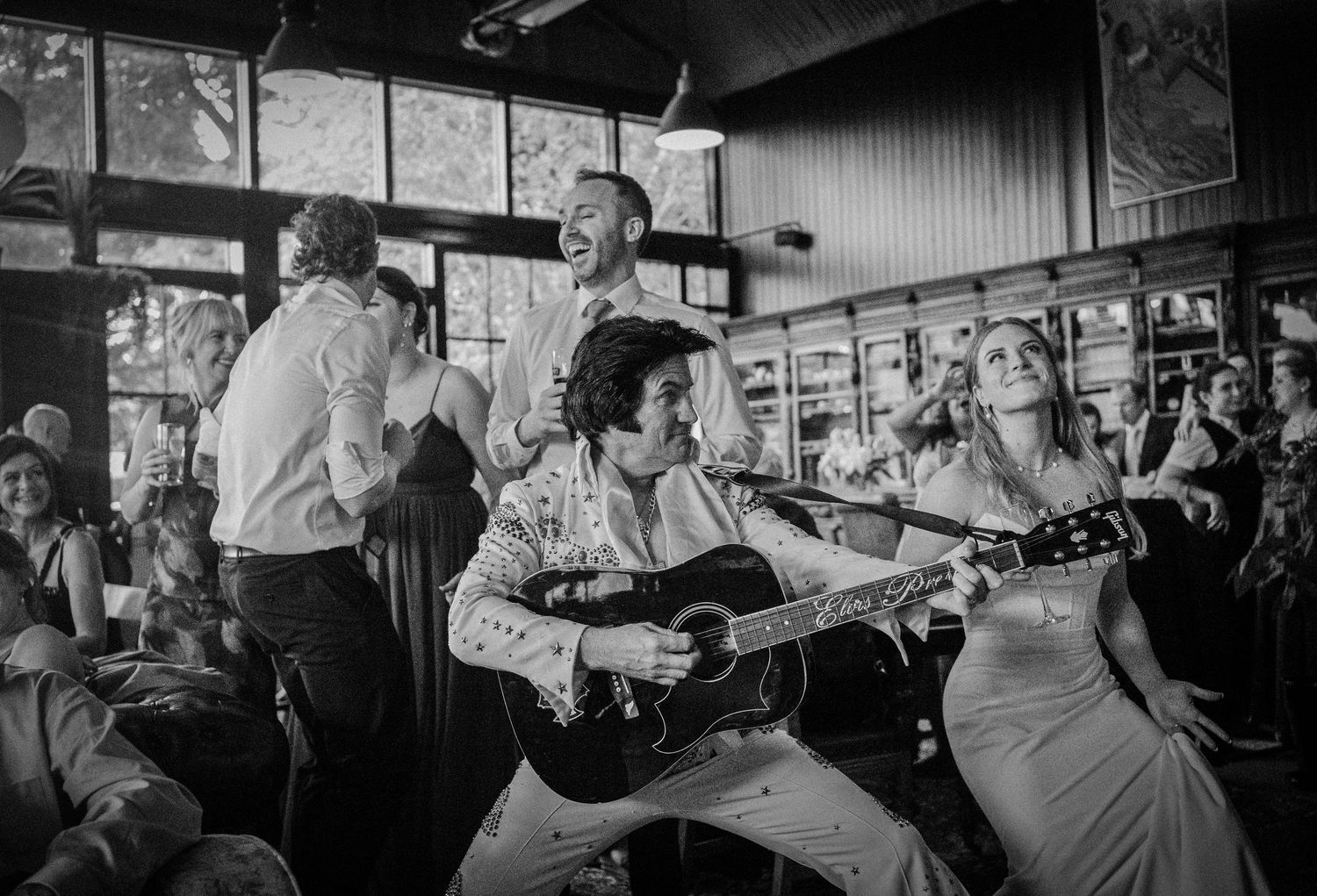 An Elvis impersonator performs with a guitar as the bride and groom celebrate at their wedding.