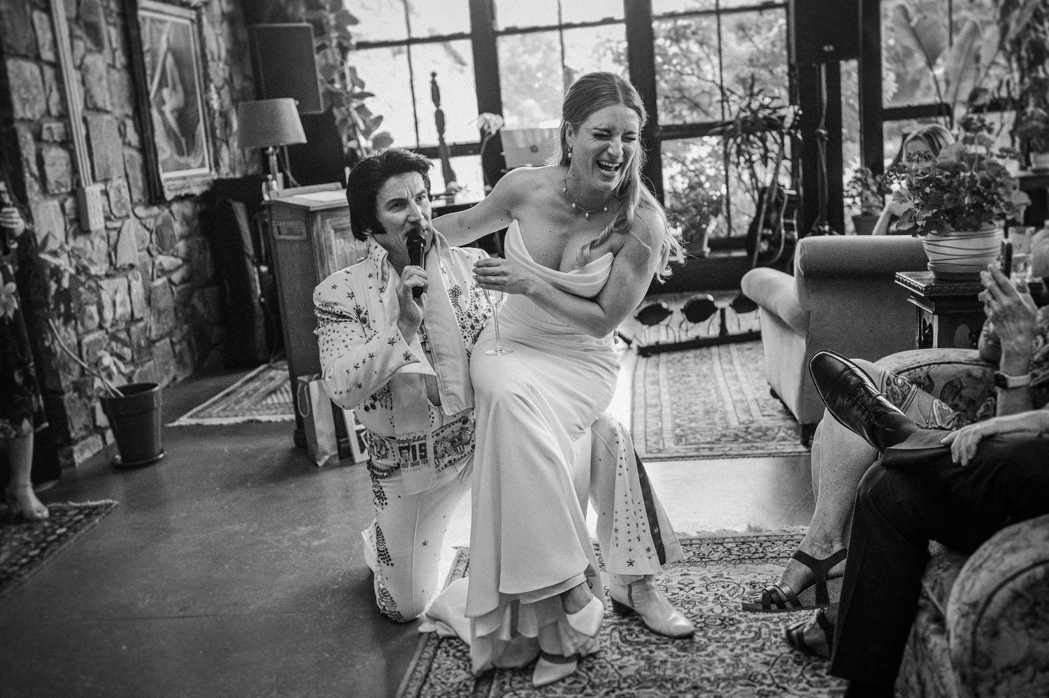 A bride laughs joyfully with an Elvis impersonator during a fun wedding celebration indoors.