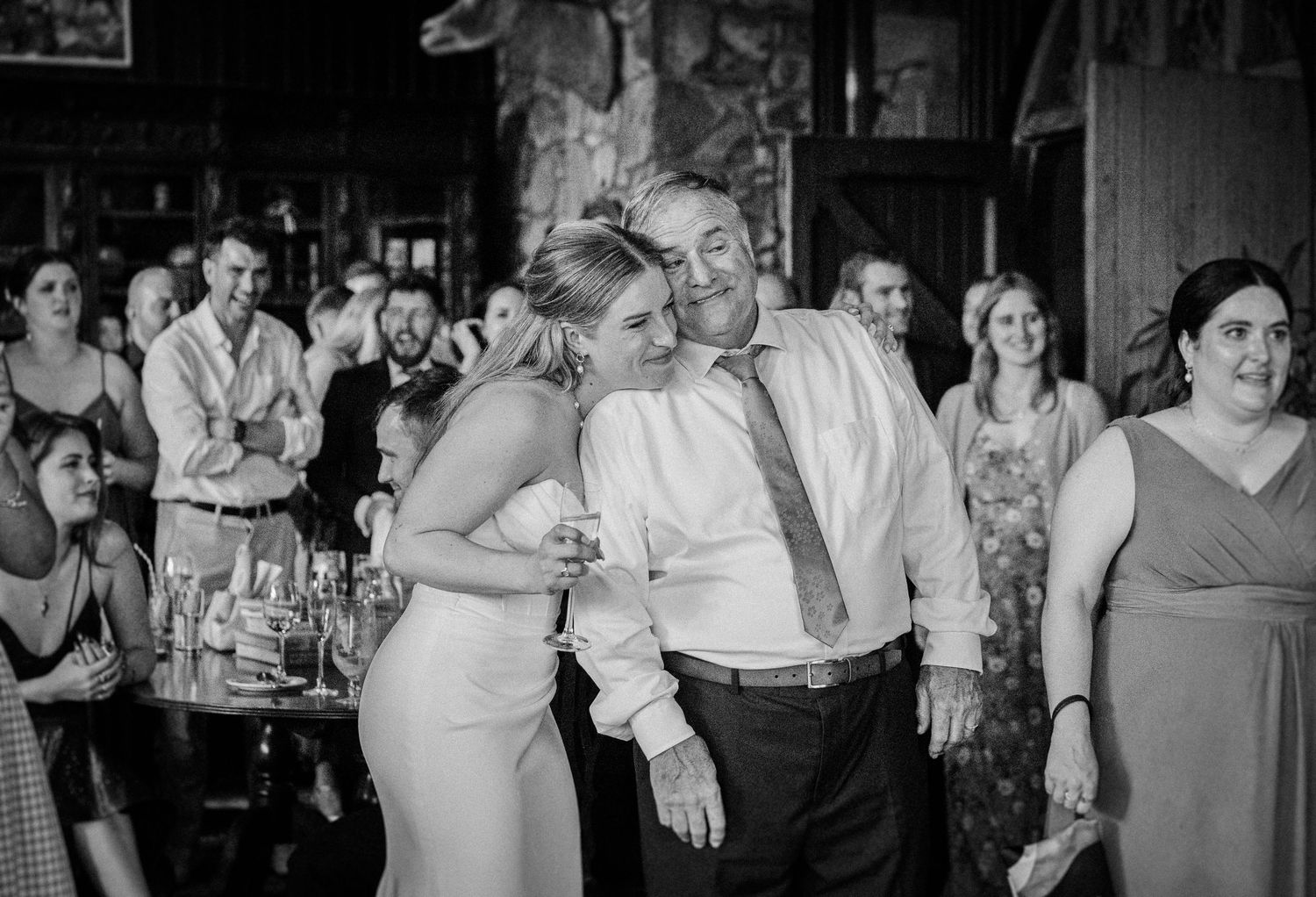 Bride and older man share a warm embrace on the dance floor at wedding reception.