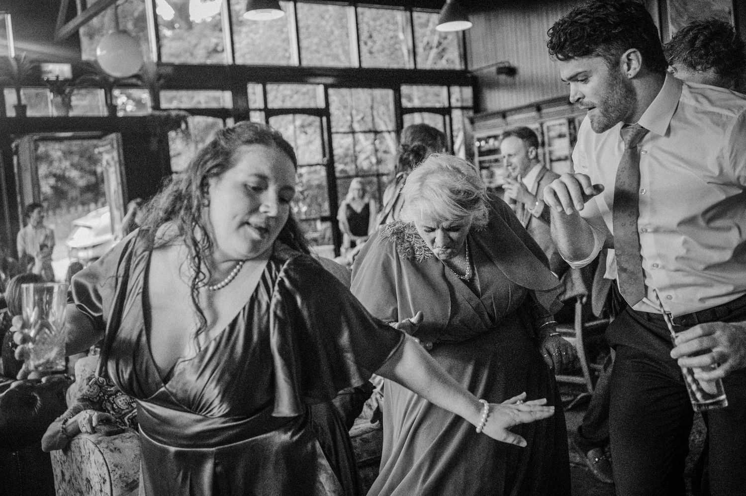 Black and white photo of wedding guests dancing joyfully at a lively indoor wedding reception celebration.