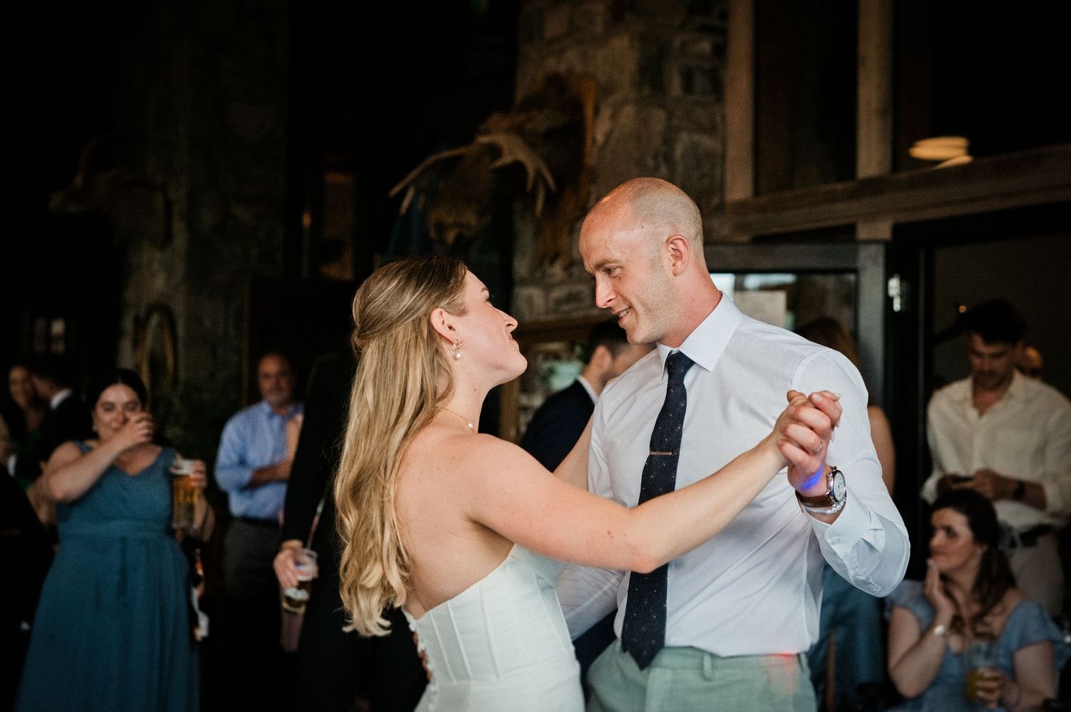 A bride and groom share their first dance surrounded by smiling guests at their wedding reception.