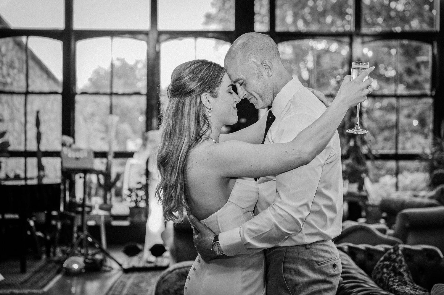 Black and white photo of a couple sharing an intimate dance, embracing closely in a warmly decorated indoor venue.