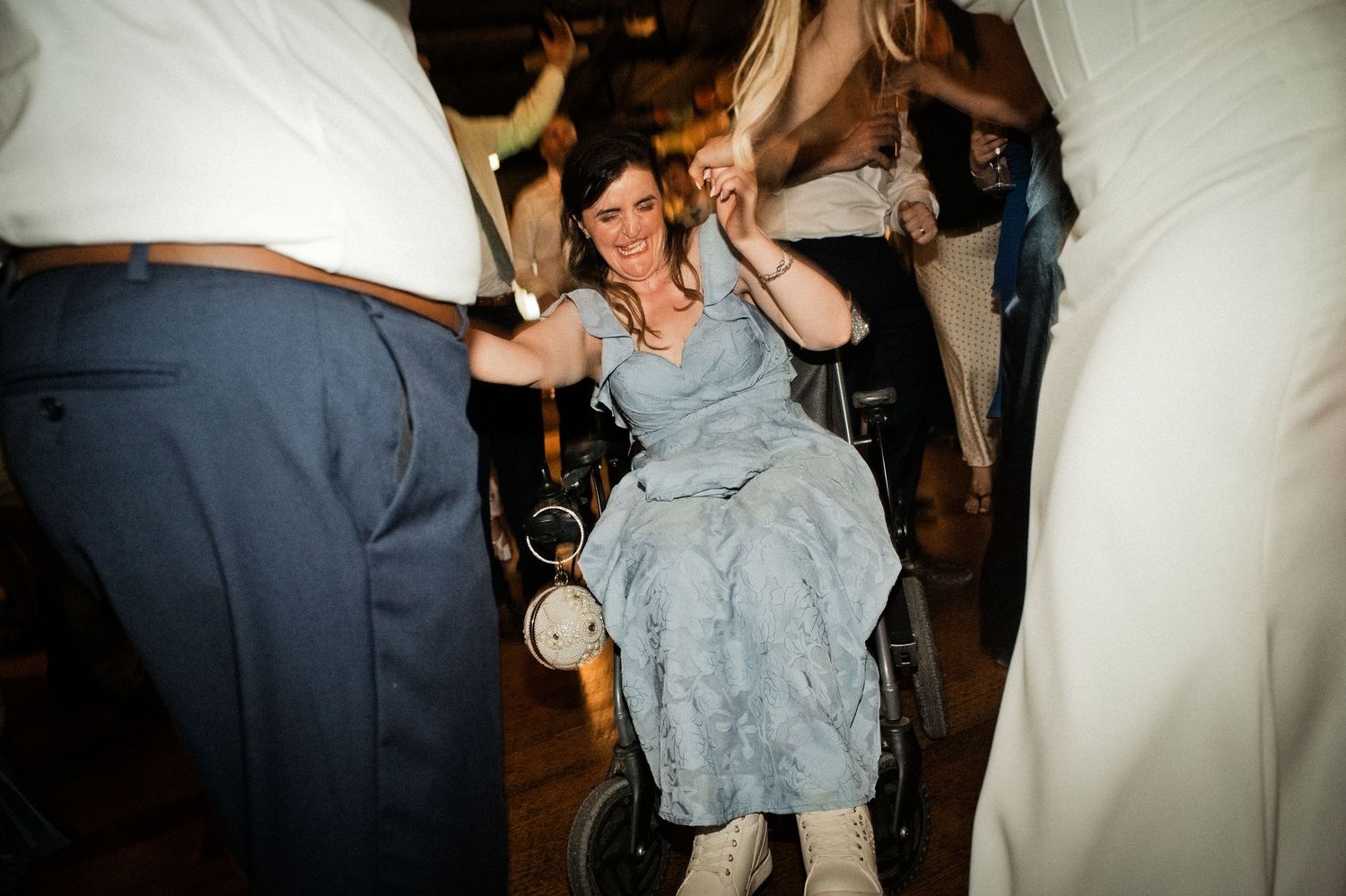Woman in wheelchair dancing joyfully at a wedding reception surrounded by guests in formal attire.