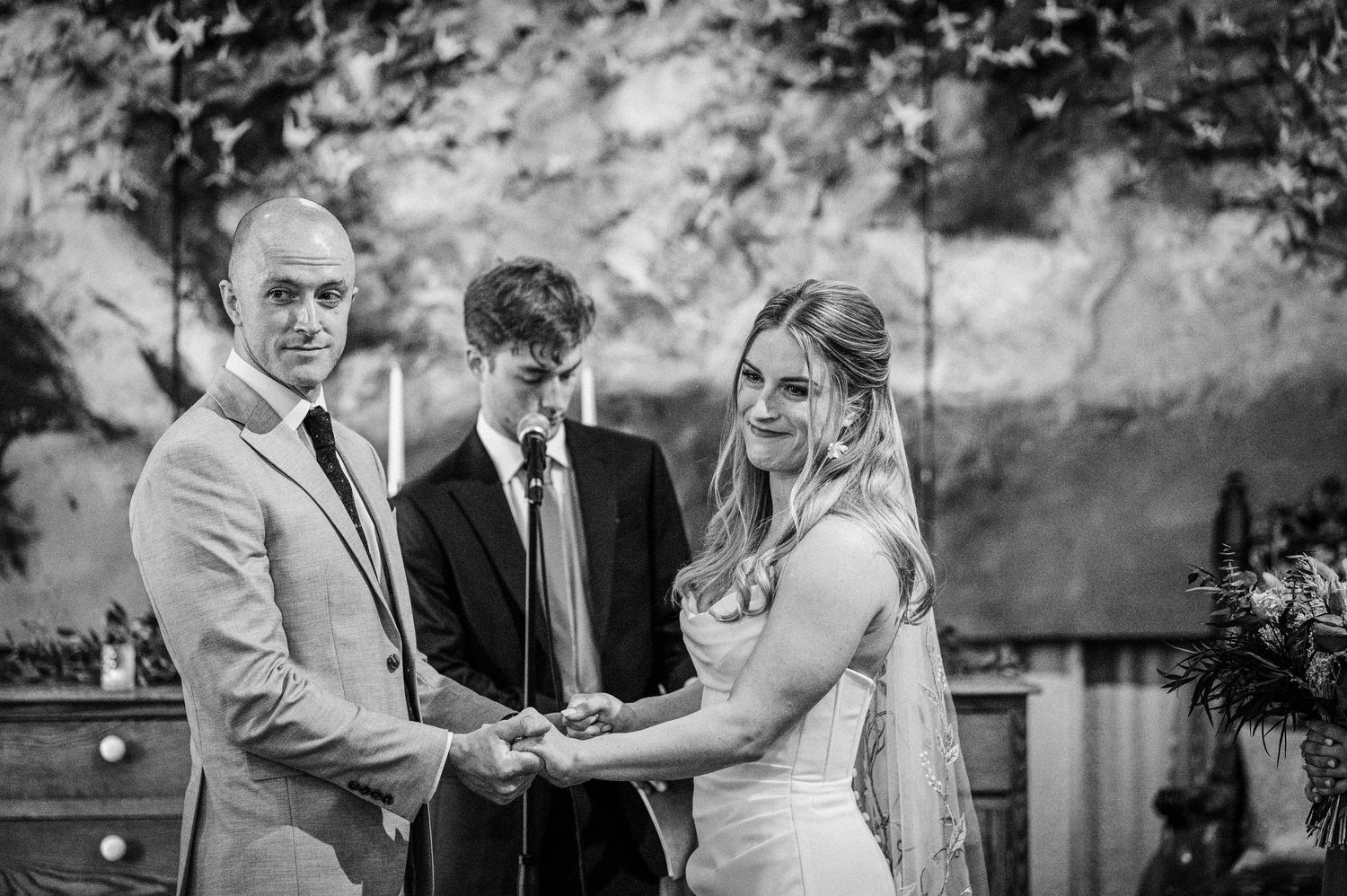 Bride and groom exchanging vows at rustic wedding ceremony, black and white photo.