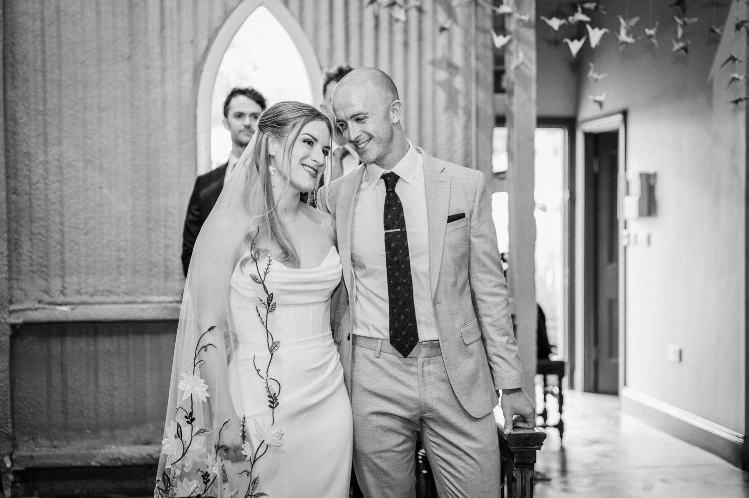 Black and white photo of smiling bride and groom walking together down church aisle after ceremony.