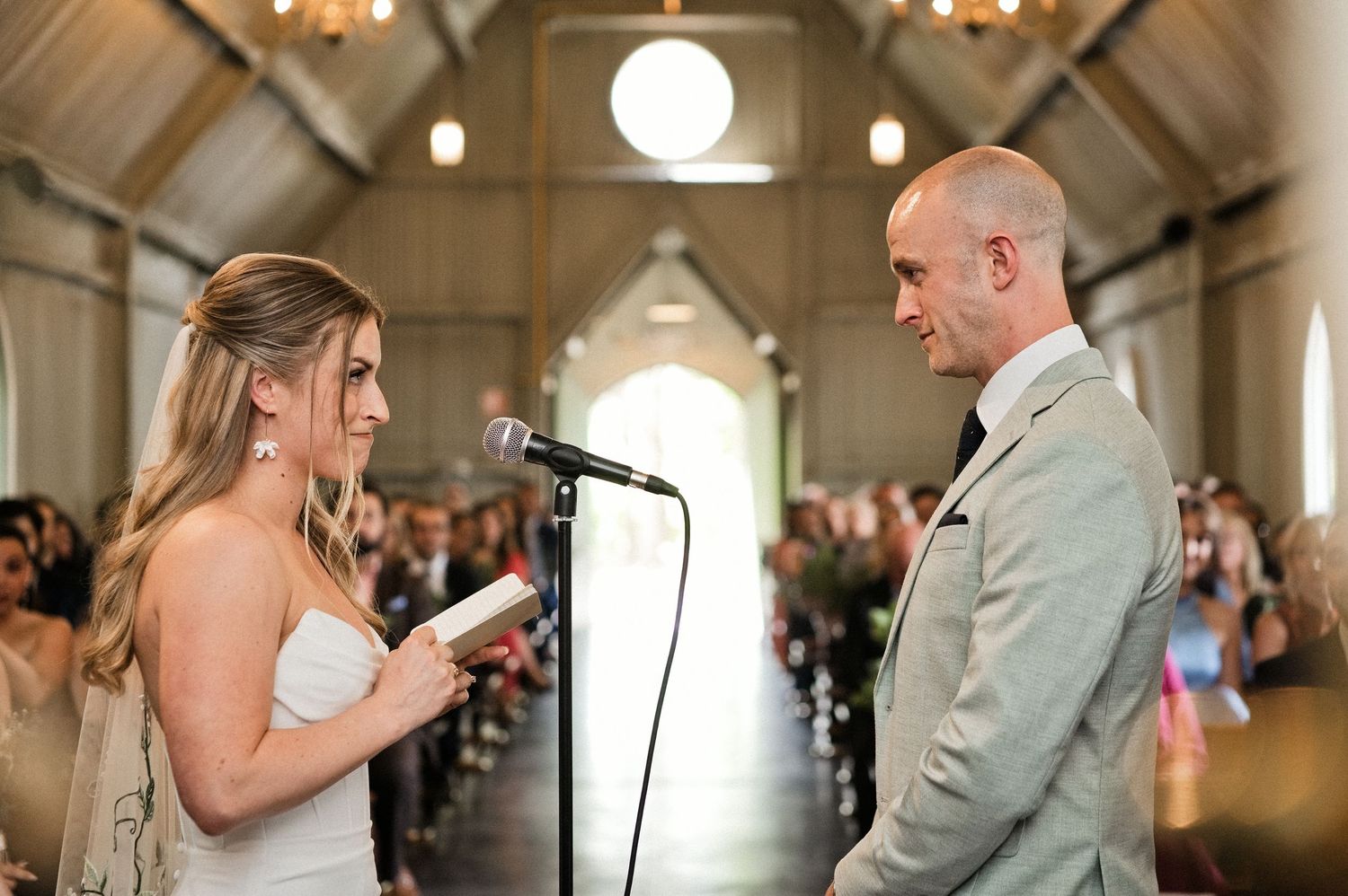 Bride reads wedding vows at microphone to groom during church ceremony.