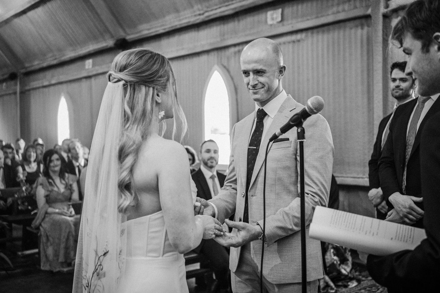 Groom smiling at bride during wedding ceremony in a rustic chapel.