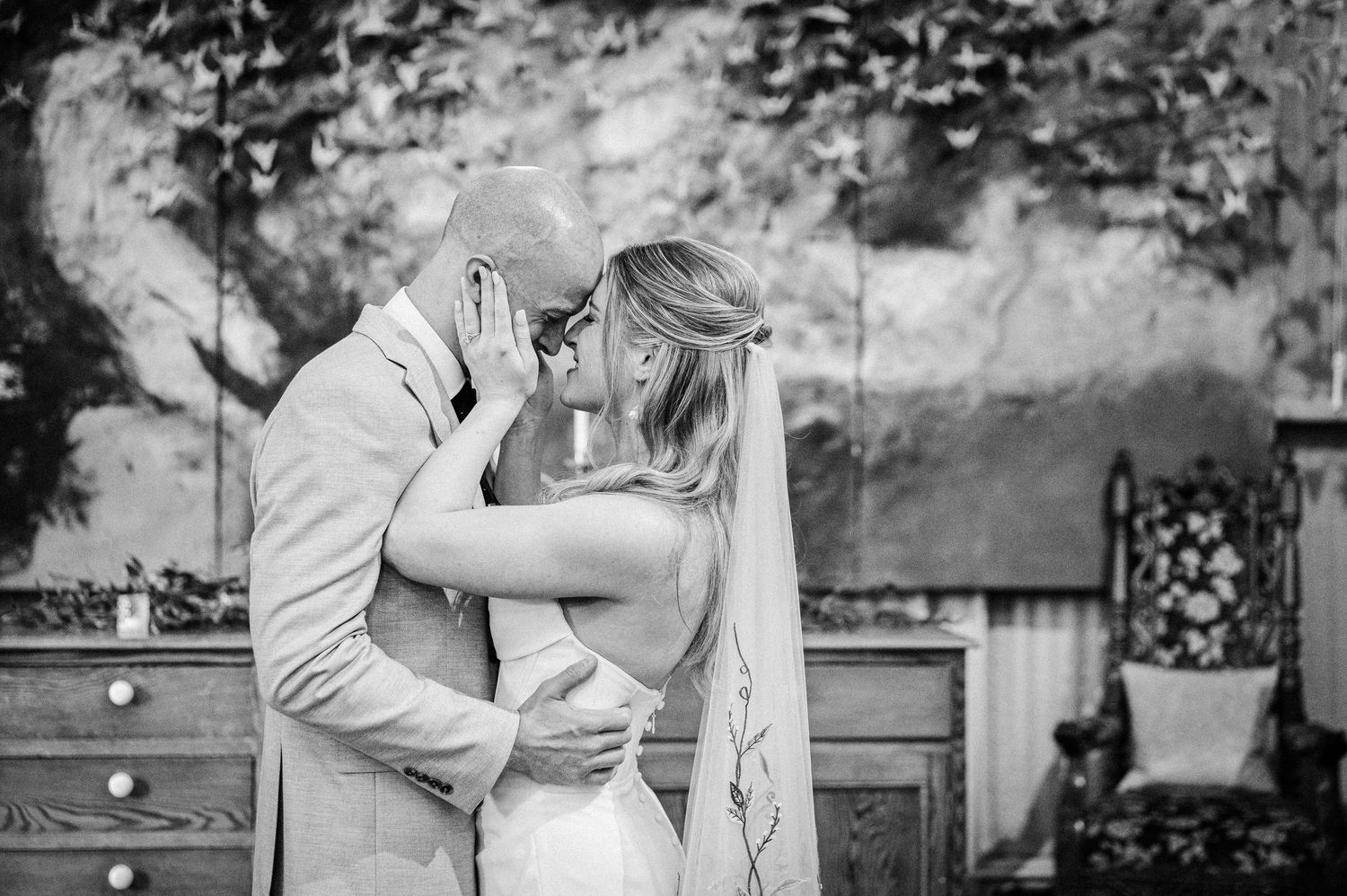 Newlyweds share their first kiss as a married couple in a romantic black and white wedding portrait.