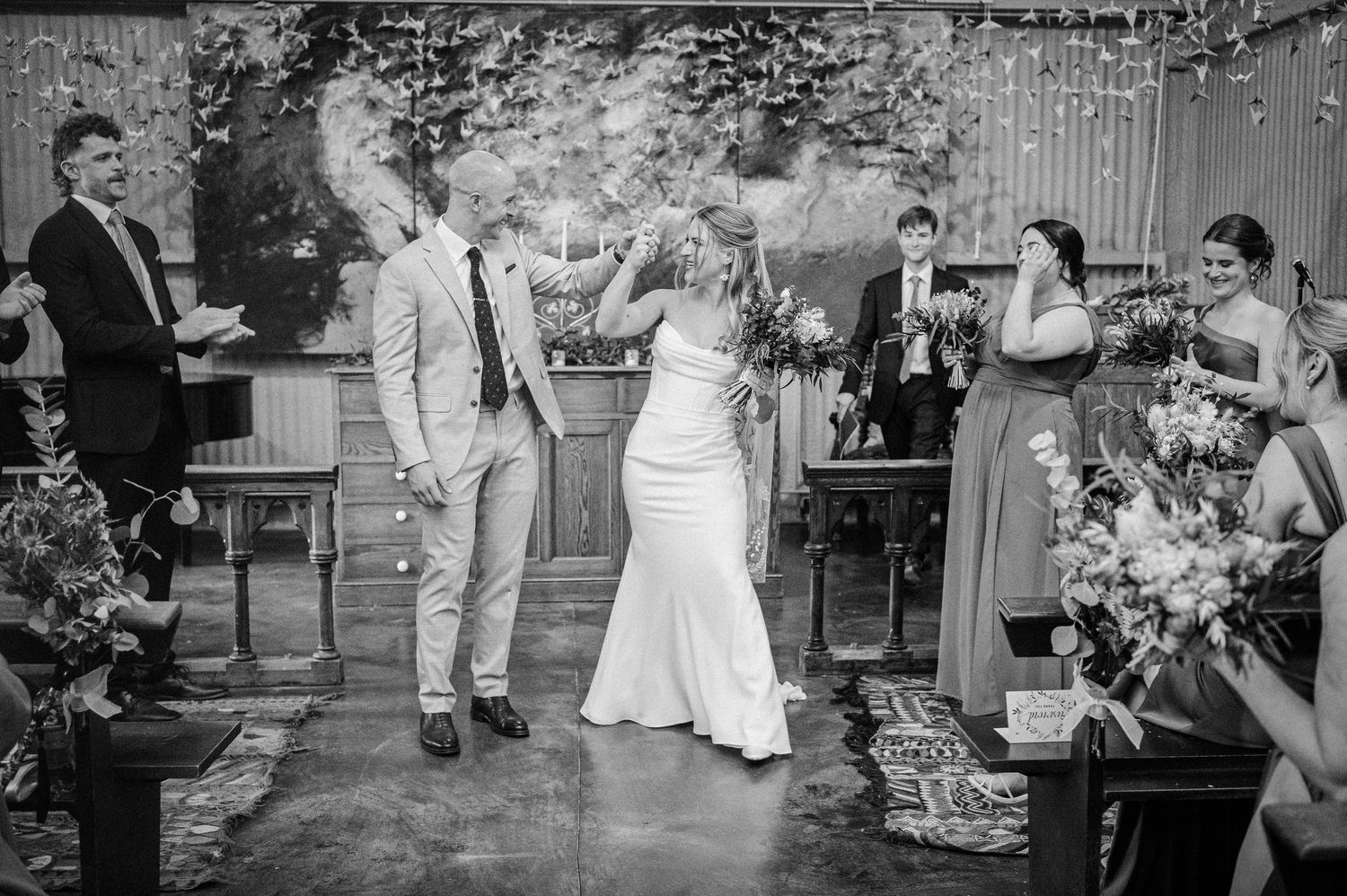 Black and white photo of bride and groom sharing first kiss at rustic wedding ceremony altar.