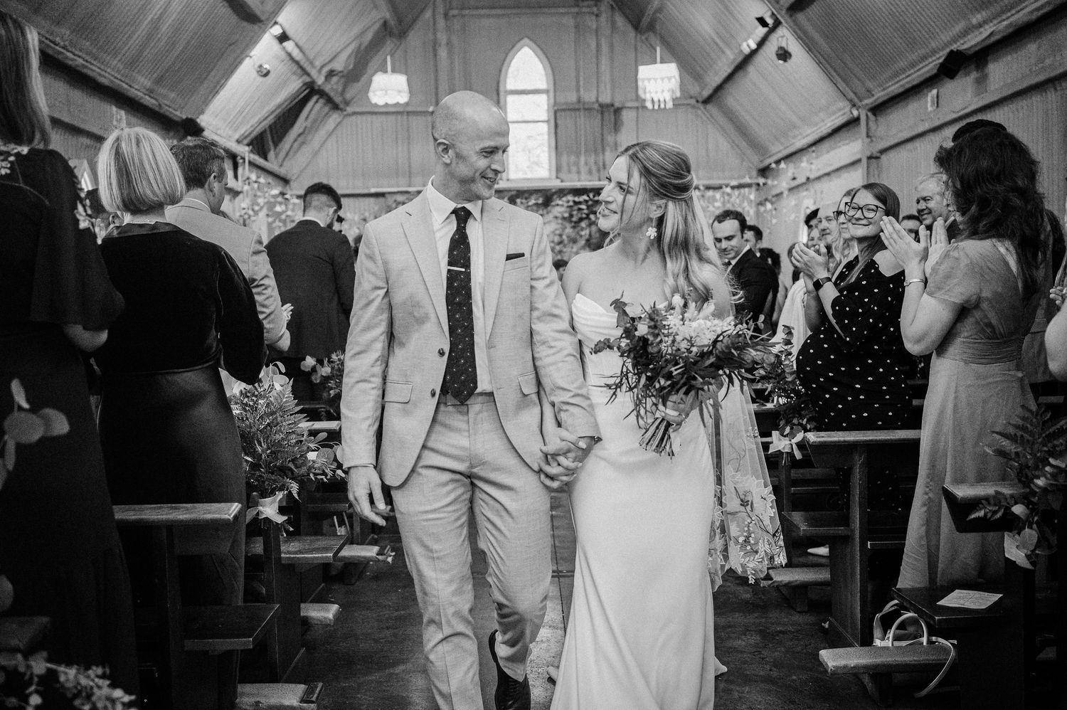 Newlyweds walking down the aisle of a rustic church after their wedding ceremony in black and white.