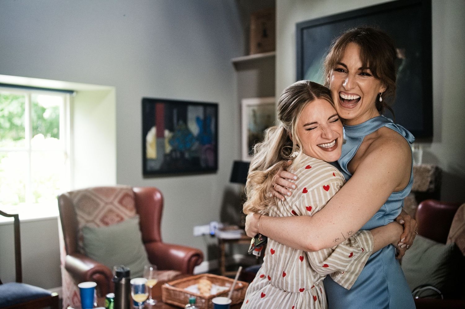 Two women sharing a joyful hug and laughing together in a bright, cozy living room setting.
