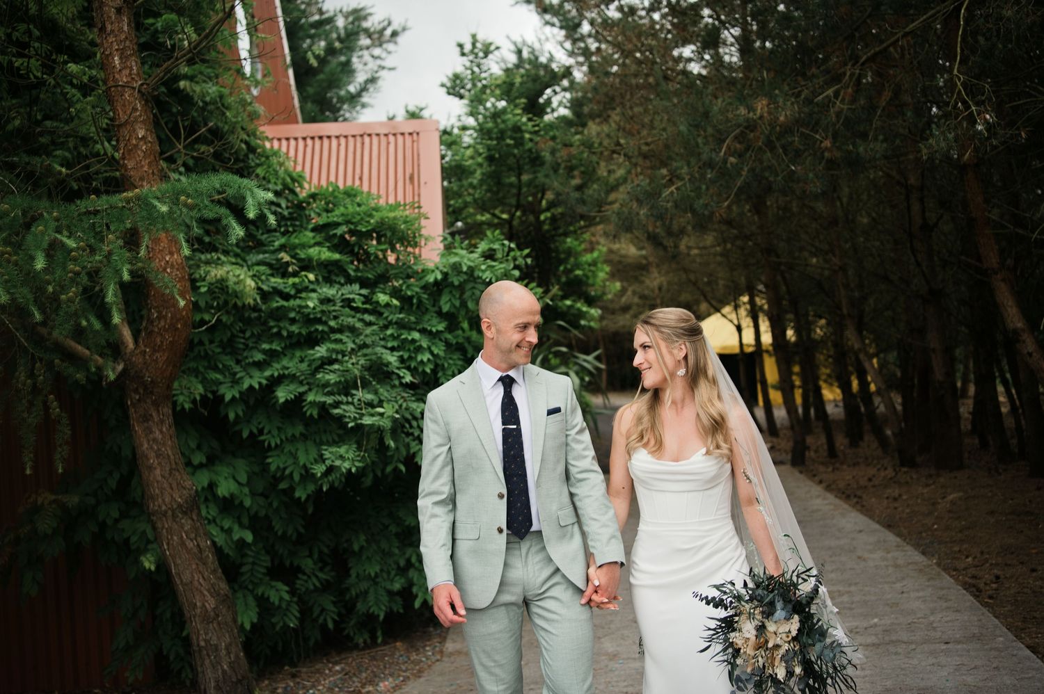Bride and groom walk hand in hand along a garden path on their wedding day.