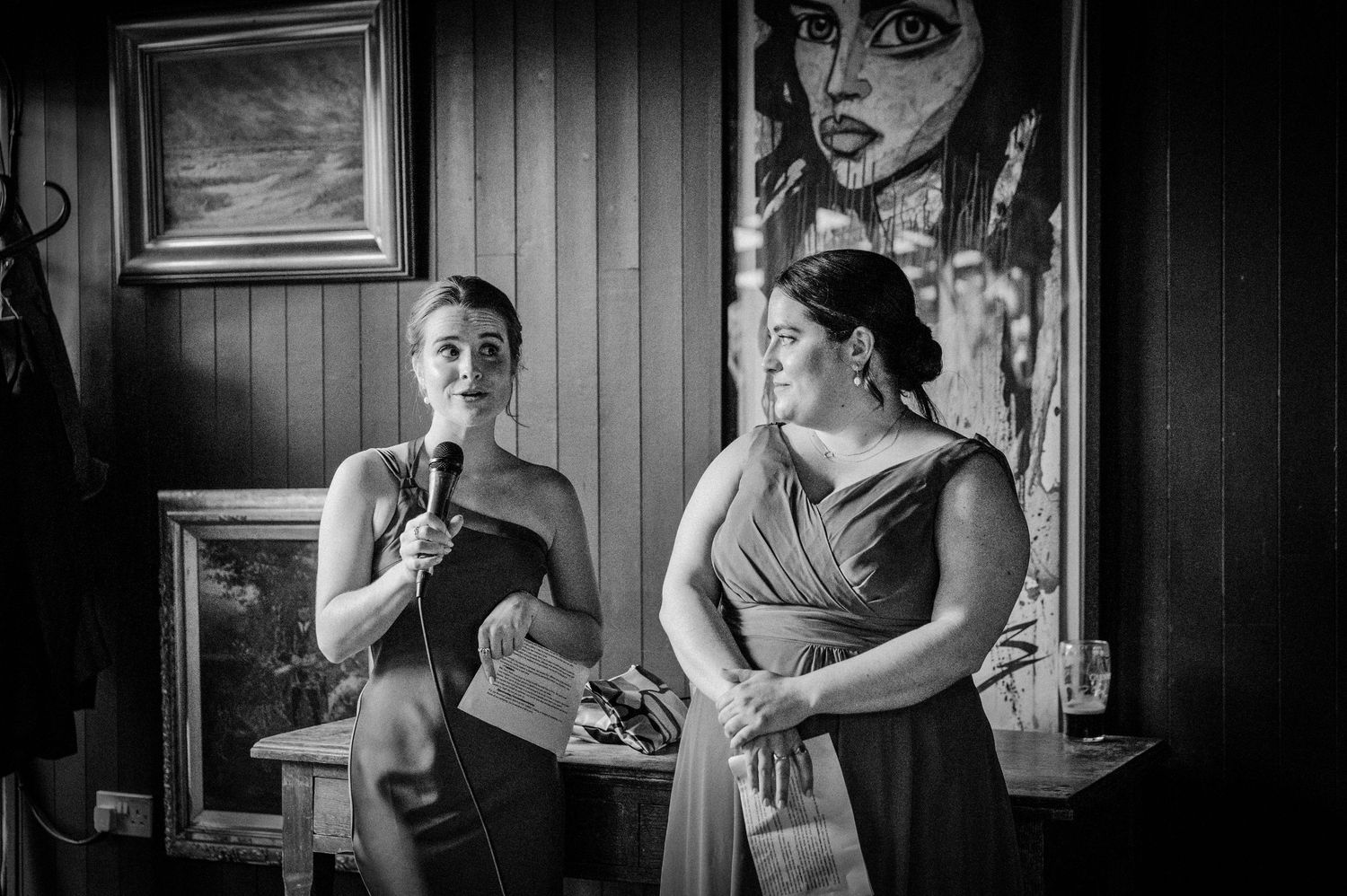 Two women in formal dresses give speeches at a wedding reception in black and white photo.