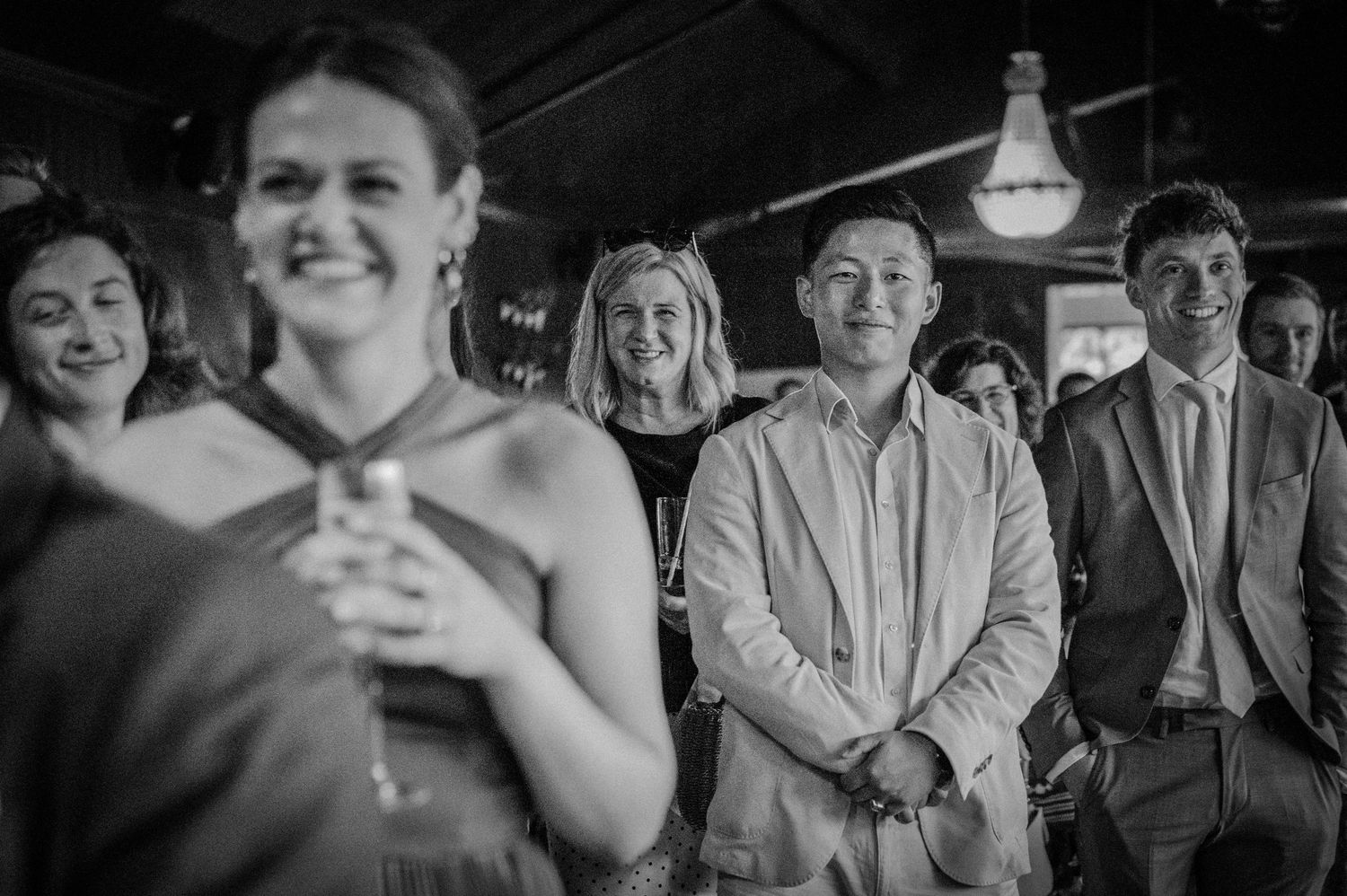 Wedding guests smile and watch ceremony in black and white candid reception photo.
