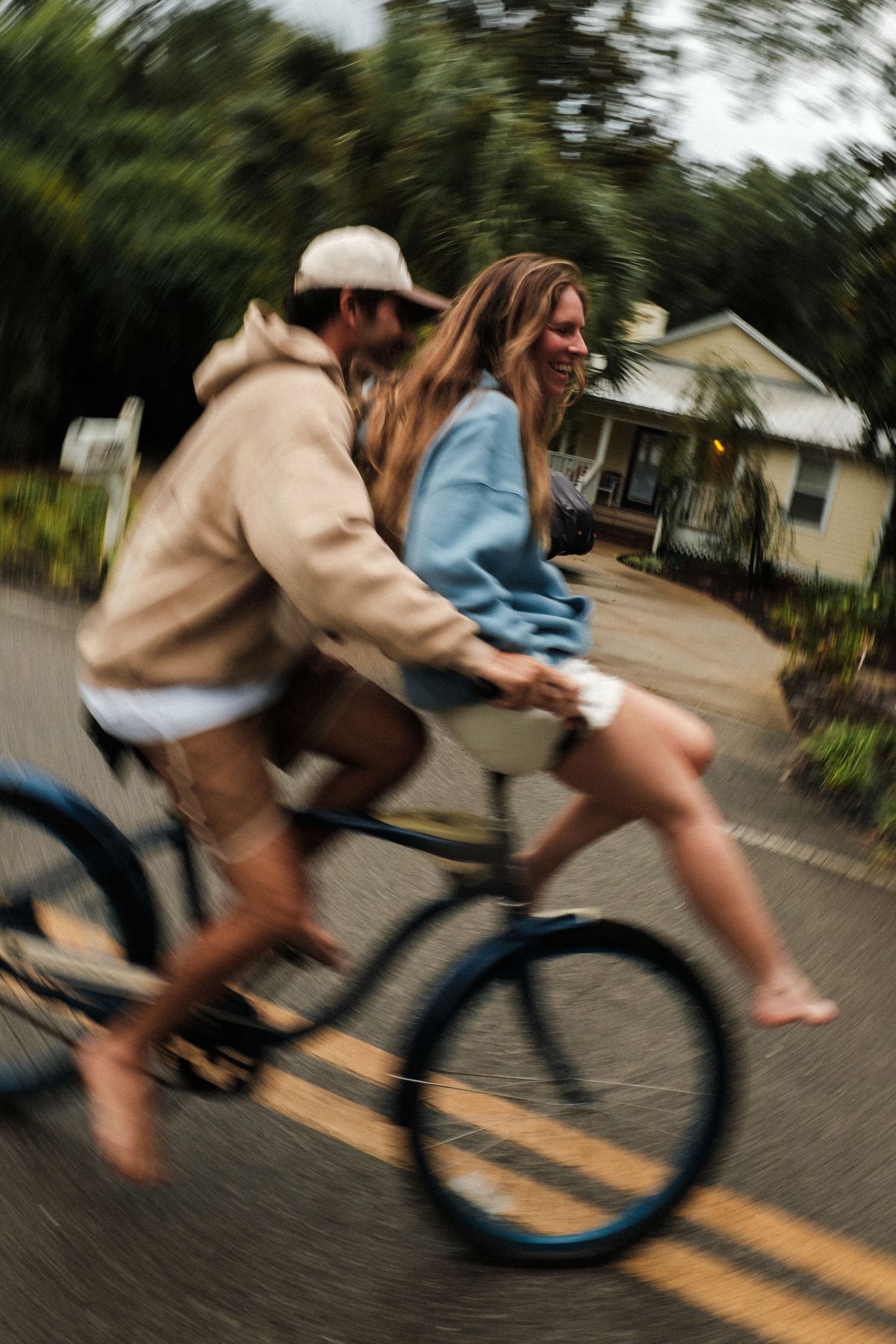 A couple rides a bicycle together on a street, laughing and enjoying the ride, with motion blur adding energy.
