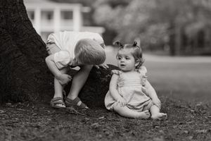 Two young children playing near a tree trunk in a park, captured in black and white photography.
