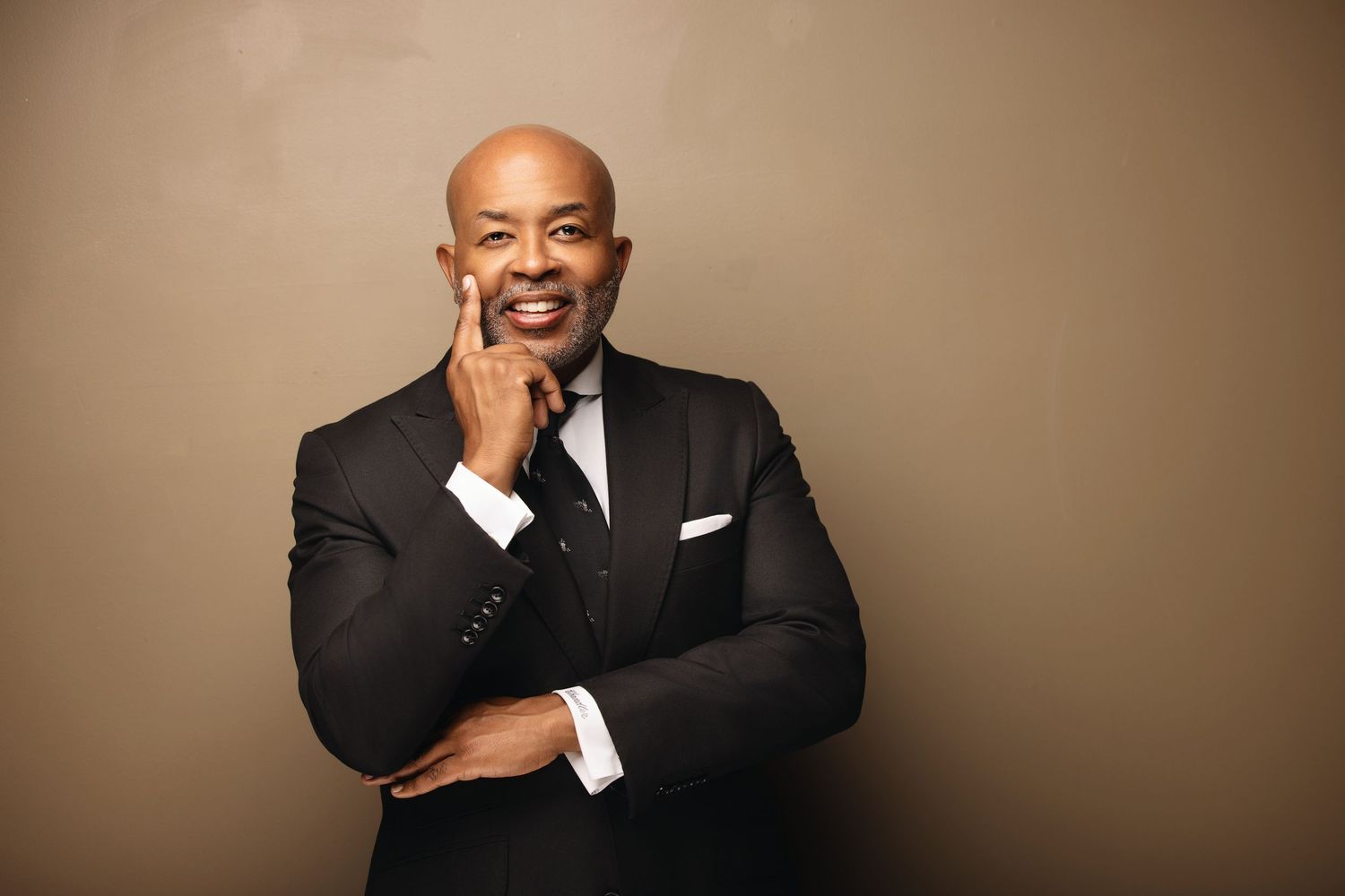 Business professional smiling warmly against a neutral beige backdrop.