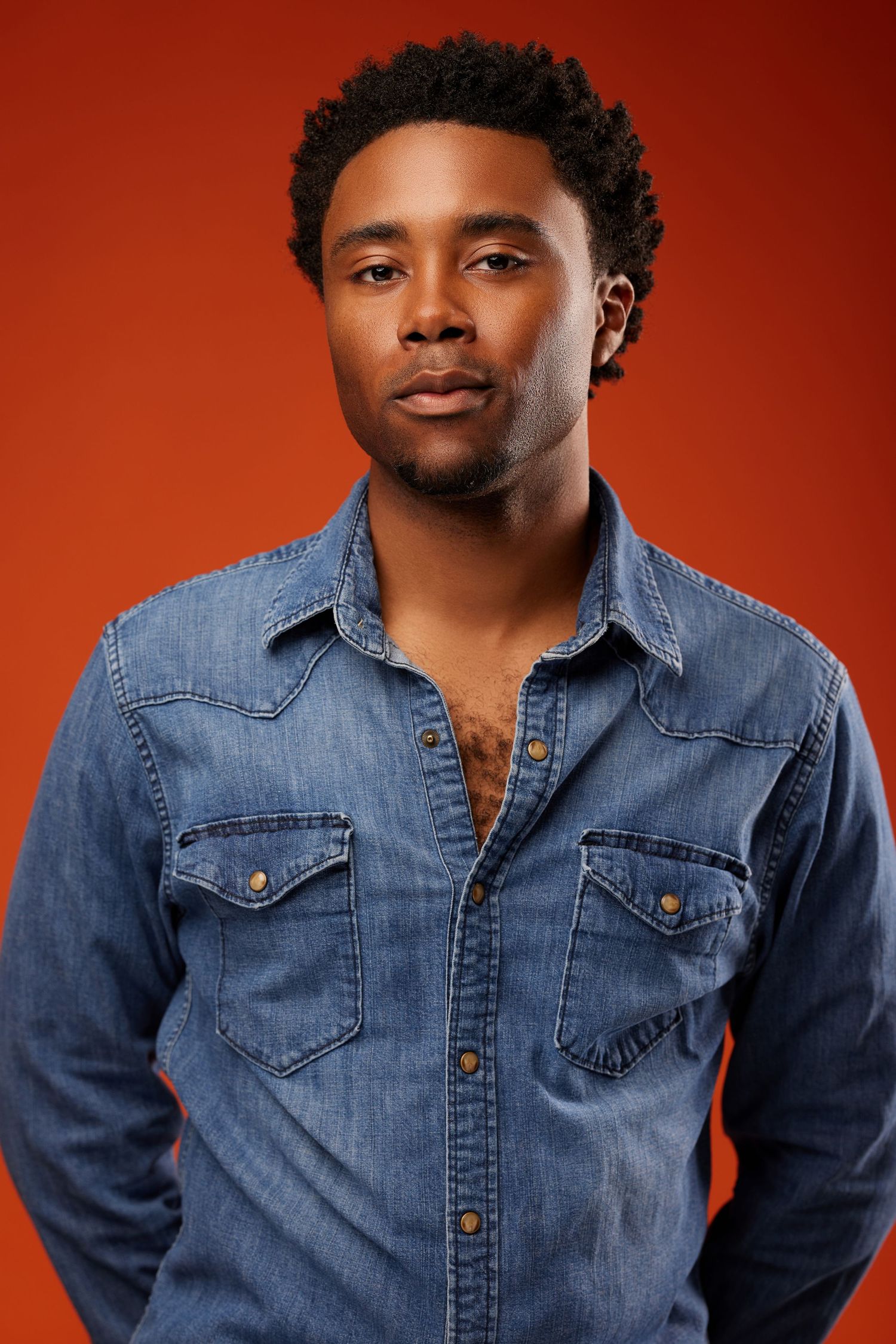Portrait against orange background of someone wearing casual denim shirt with natural hair.