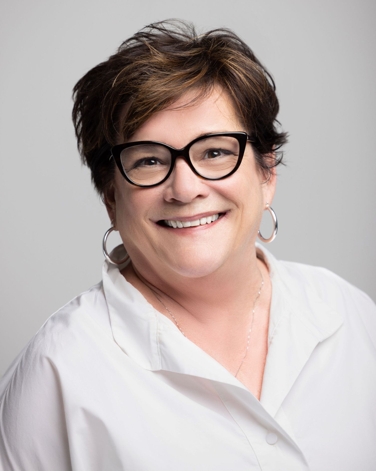 Portrait of person in white collared shirt with glasses smiling against light gray background.