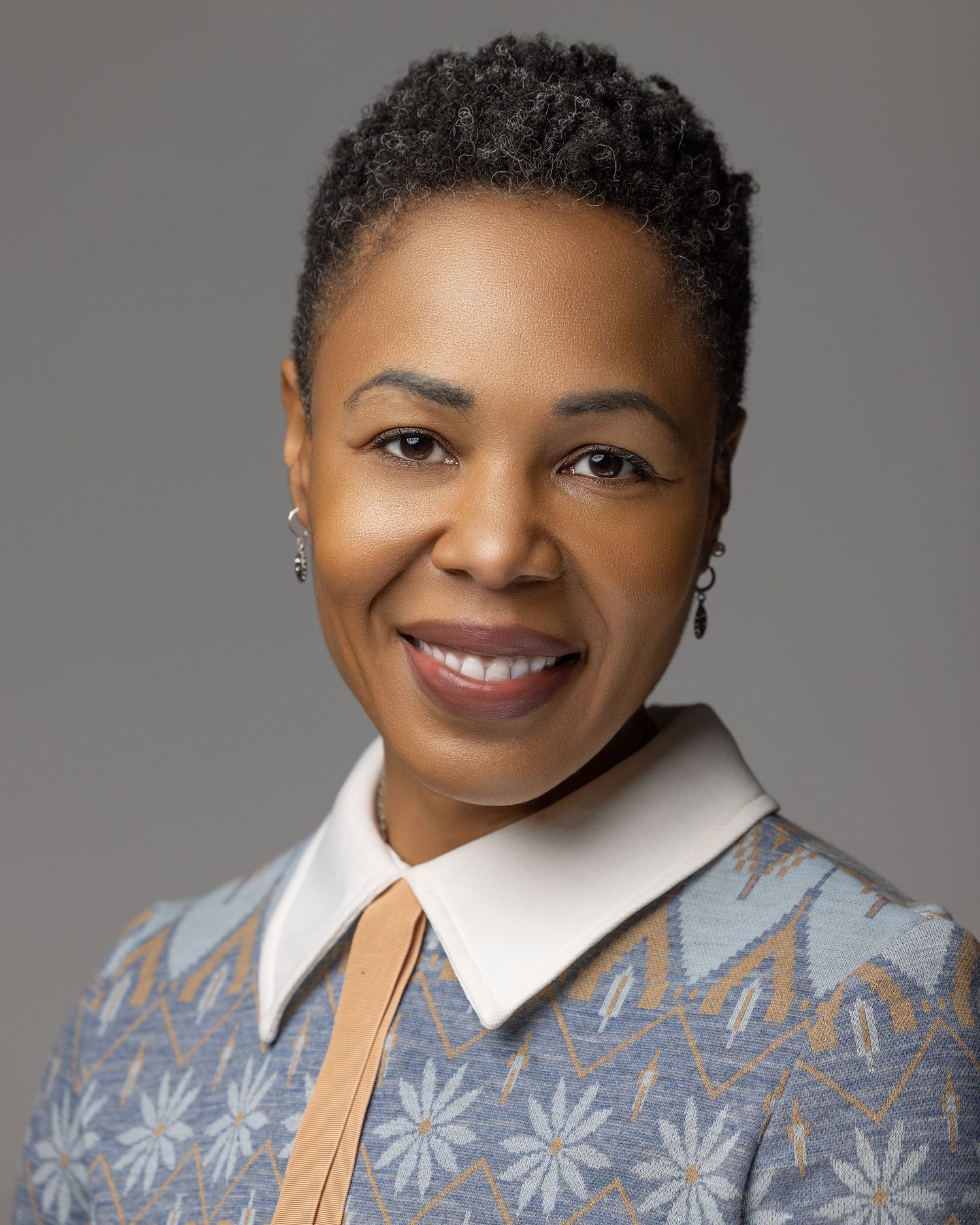 Professional portrait showing person in patterned top with light collar against gray backdrop.