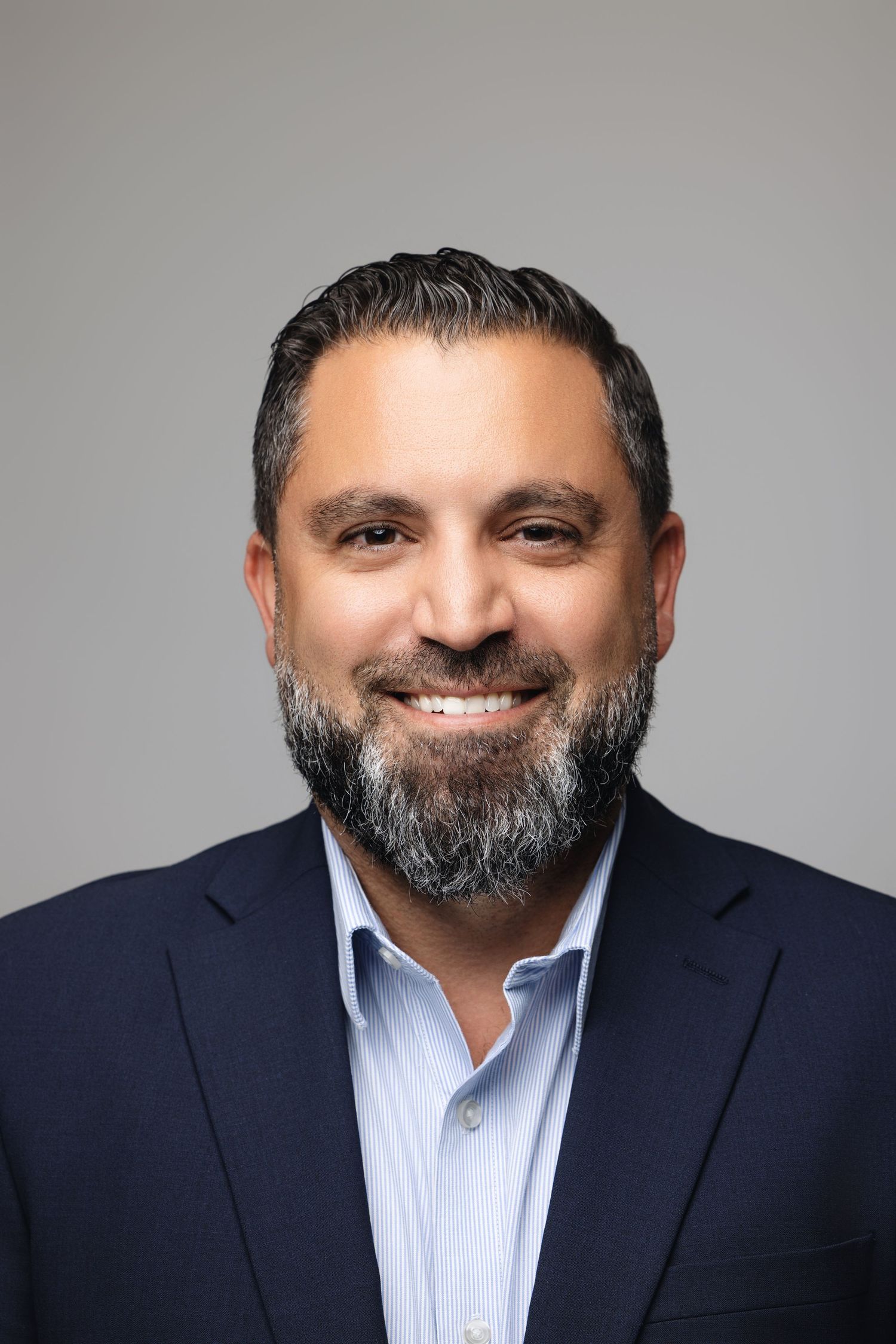 Business portrait showing person in navy blazer and light blue shirt against gray background.