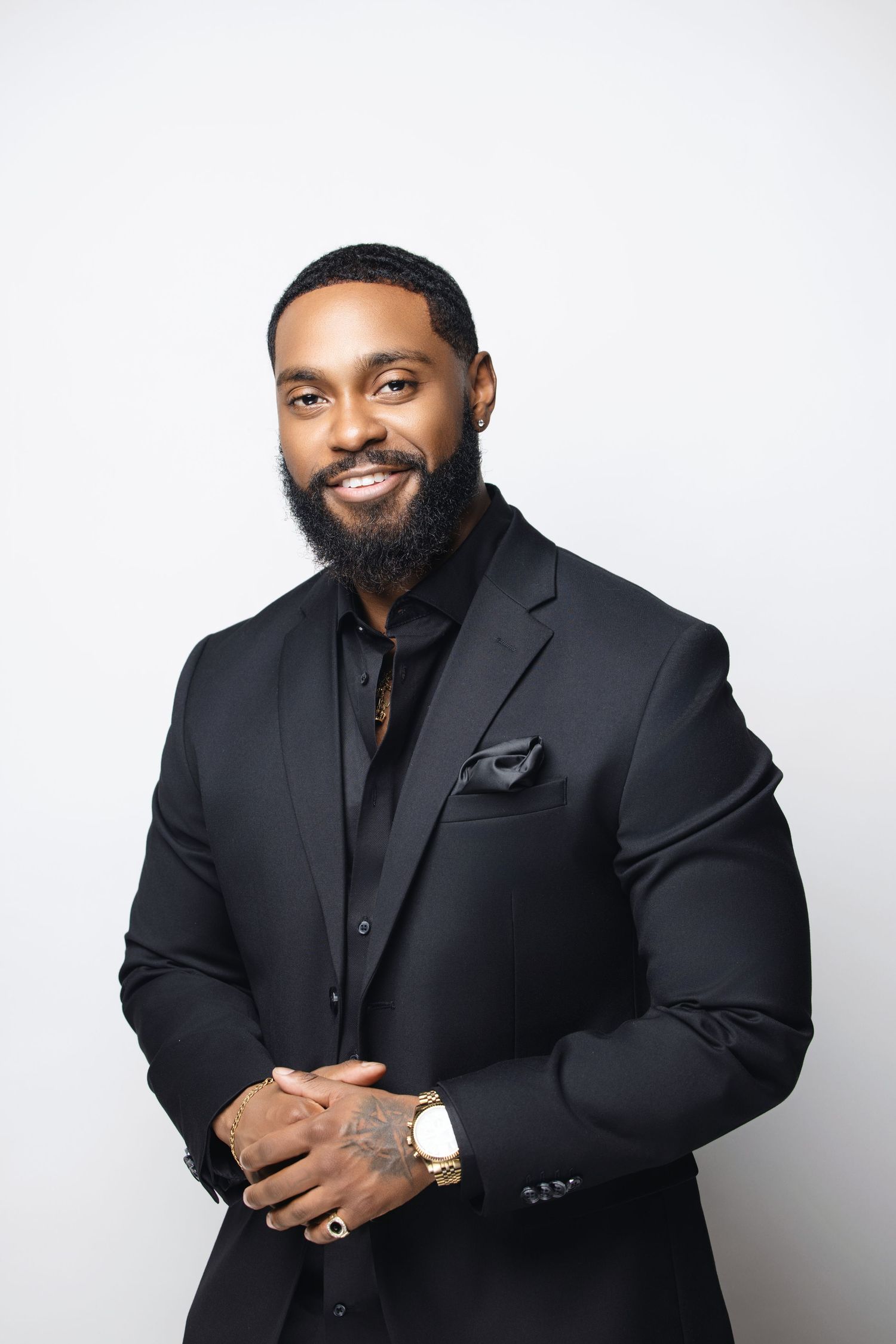 Person in black suit and shirt poses professionally against white background.