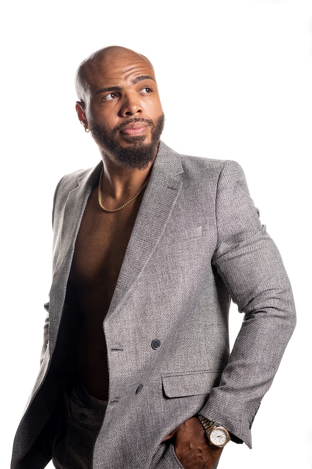 Confident bald Black man with beard wearing gray blazer and gold watch poses against white background. Gerardo & CO. portraits