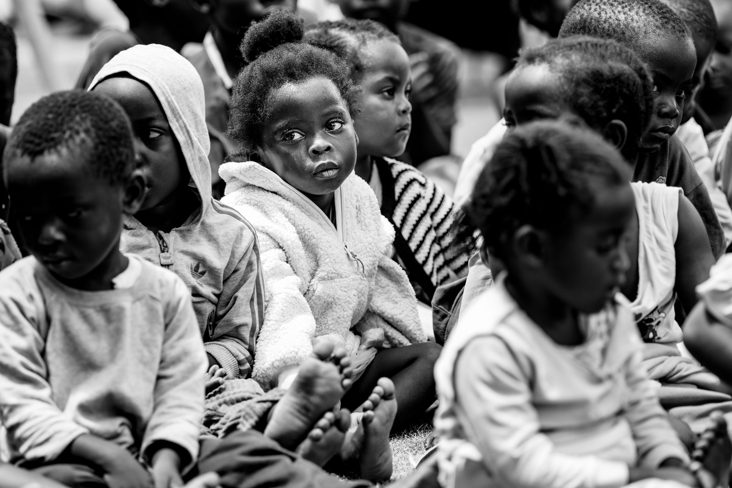 Black and white photo of African children sitting together, with a young child in a jacket looking directly at the camera.