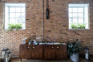 Rustic brick wall interior with wooden sideboard, potted plants, two windows, and decorative lanterns in a stylish loft space.