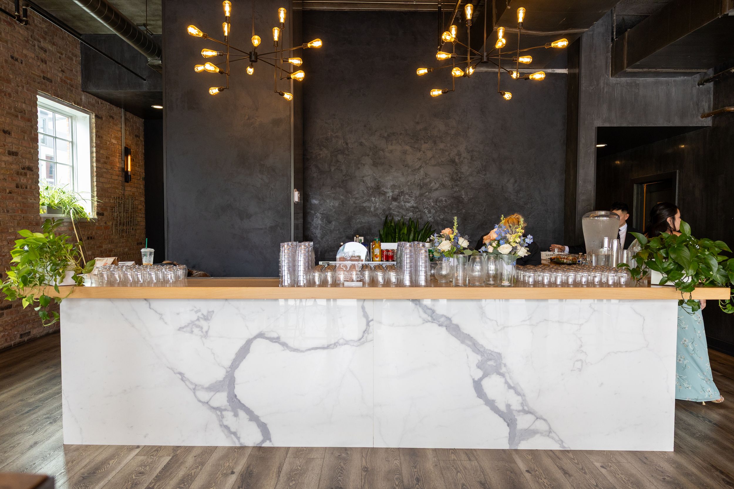 Elegant marble bar with gold pendant lights in a modern industrial venue with exposed brick walls.