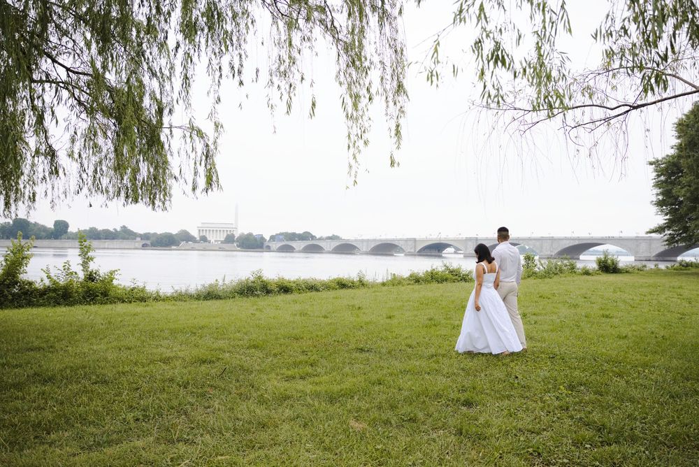 Bride and groom embrace on green lawn by the Potomac River with the Arlington Memorial Bridge in the background.