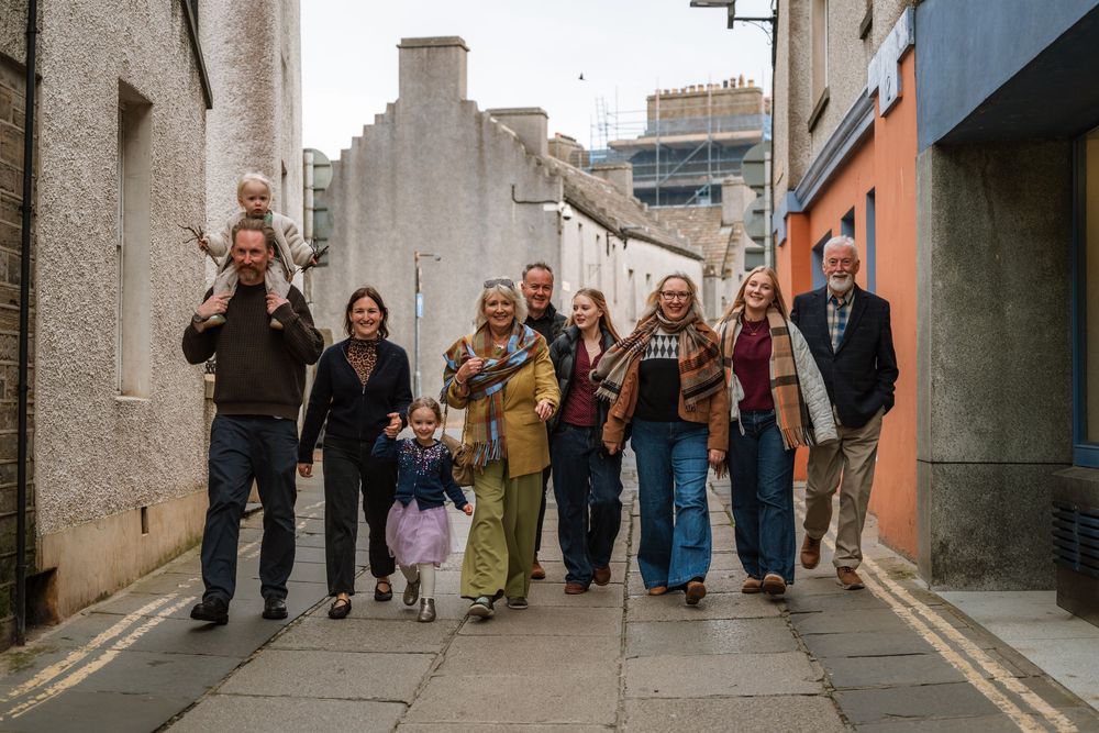 Large multigenerational family walking together down a narrow cobblestone alley in a quaint European town.