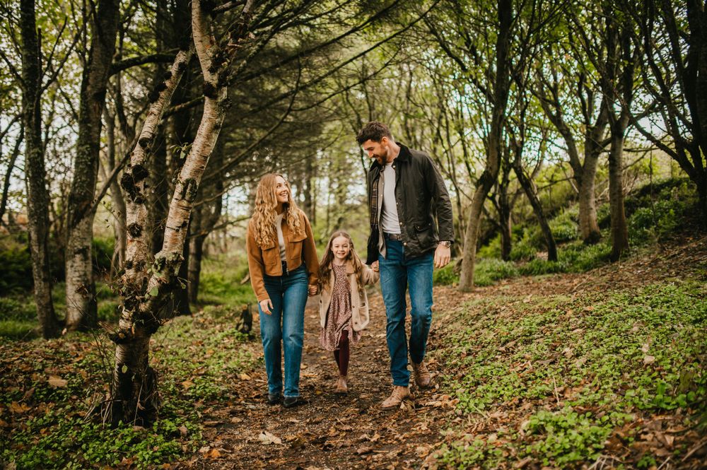 A family walks together holding hands along a wooded trail on an autumn day in nature.