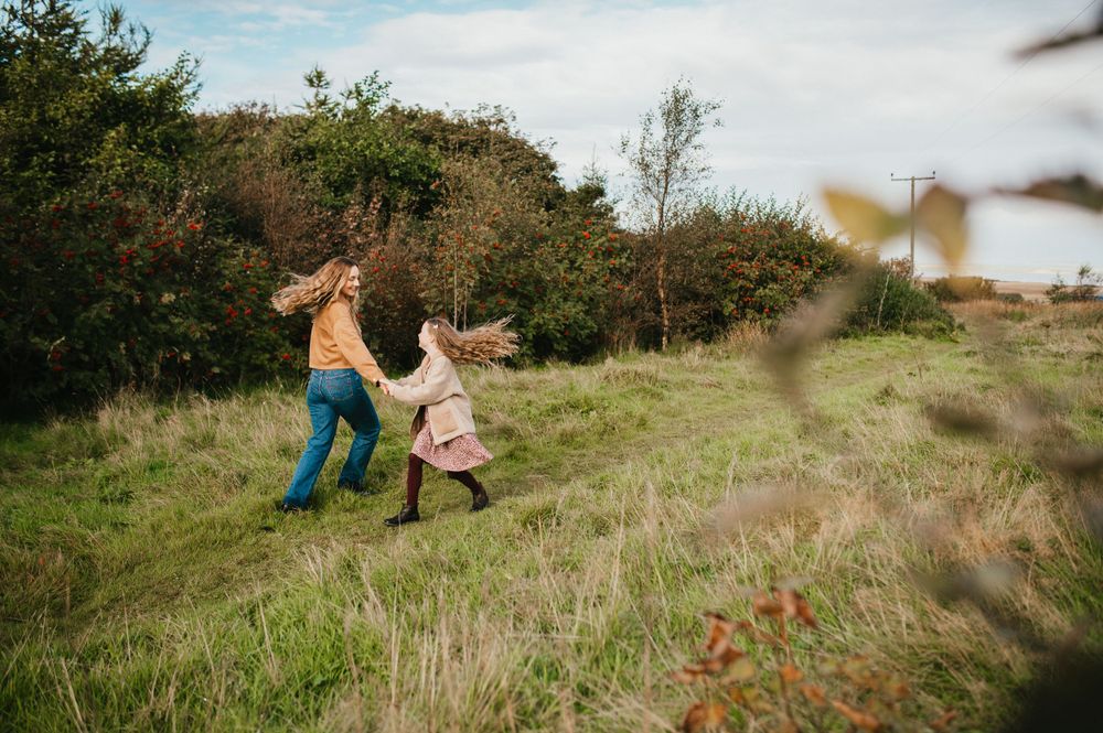Two people hold hands and run through a grassy hillside meadow on a sunny autumn day.